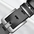 Close-up of a black leather belt with silver buckle on a light gray background