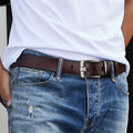 Close-up of a person wearing blue jeans with a brown belt and white shirt.